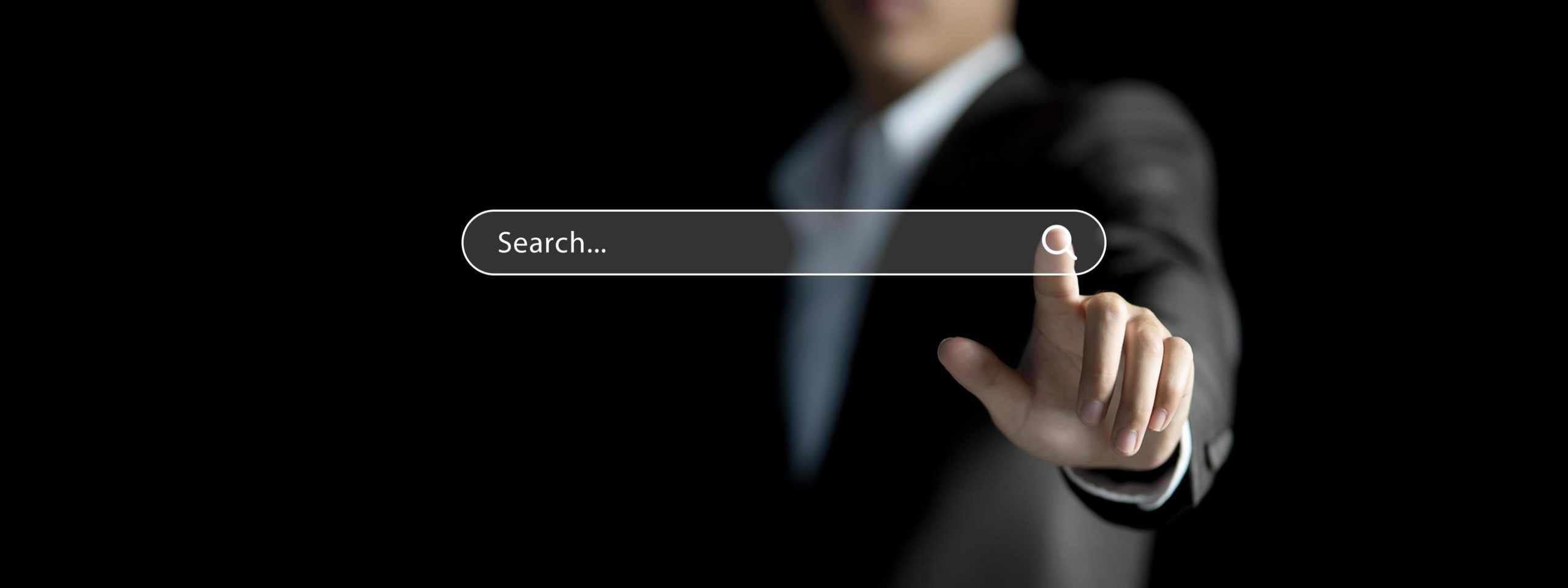 Person in a suit pointing at a virtual search bar interface on a dark background.