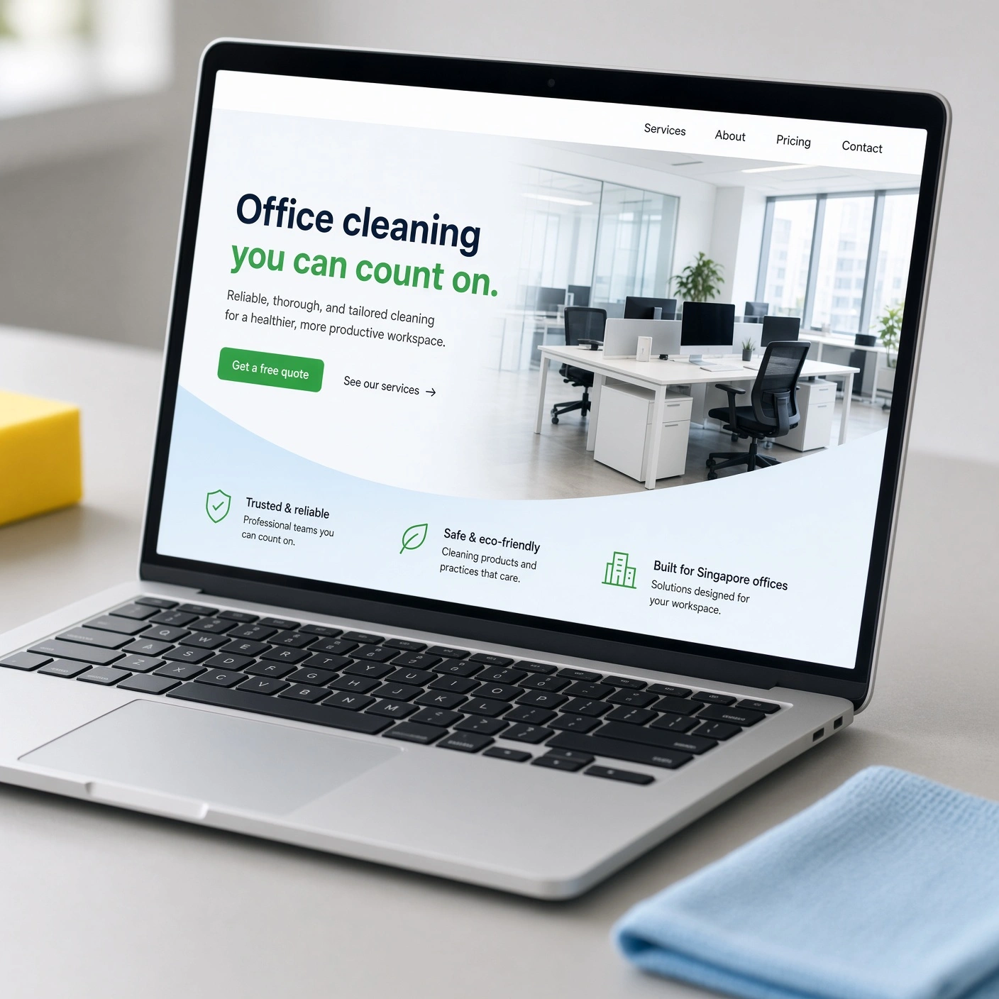 Close-up of a laptop showing a Singapore office cleaning company website, with a microfibre cloth beside it